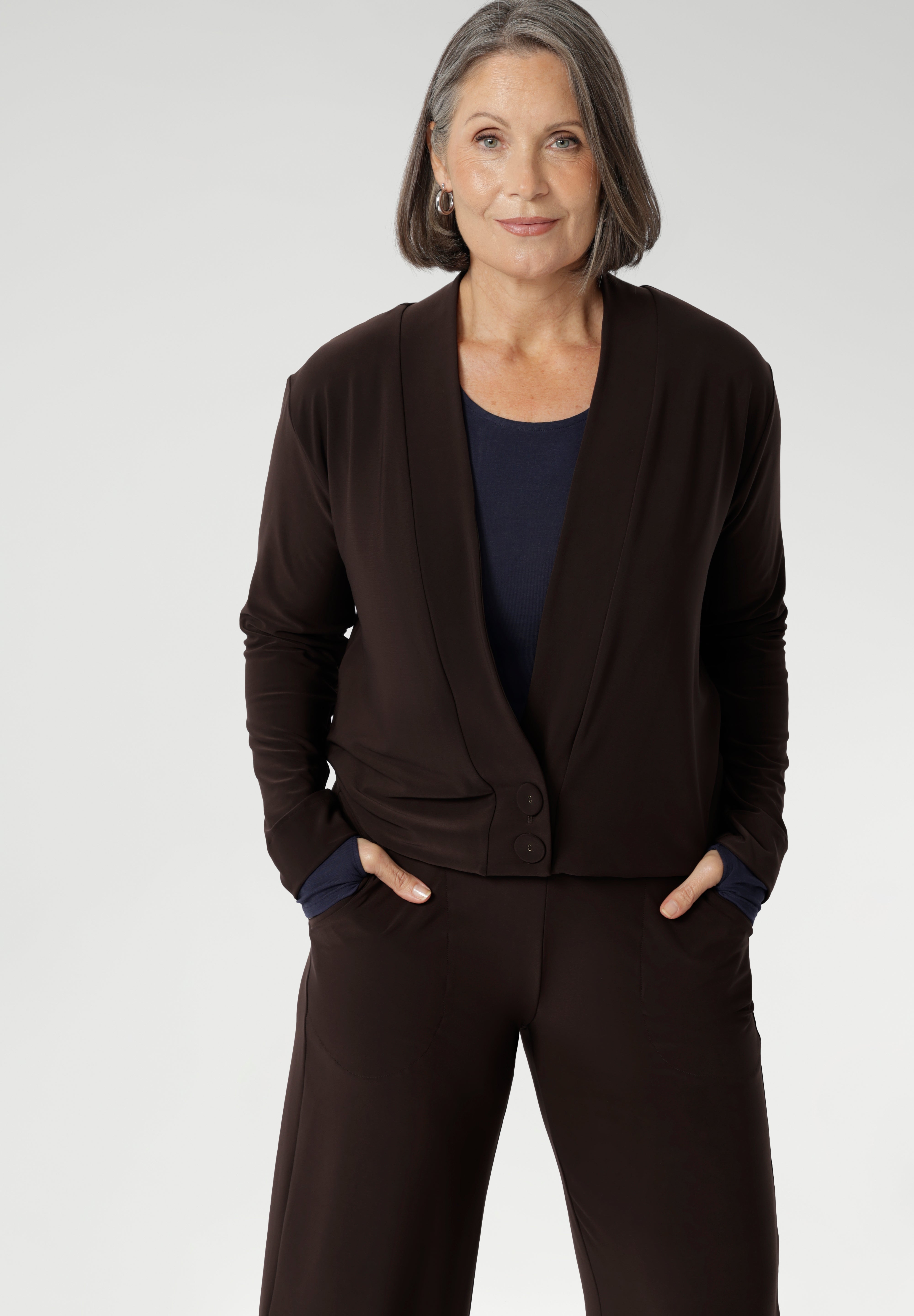 Mature aged woman wears the Sandro Jacardi in Cocoa which is a jacket-like cardigan that effortlessly adds layered dresses, making it an essential piece in our Fluid Suiting collection. Crafted from a heavyweight dry-touch jersey fabric with a soft stretch, this cardigan offers both comfort and structure.