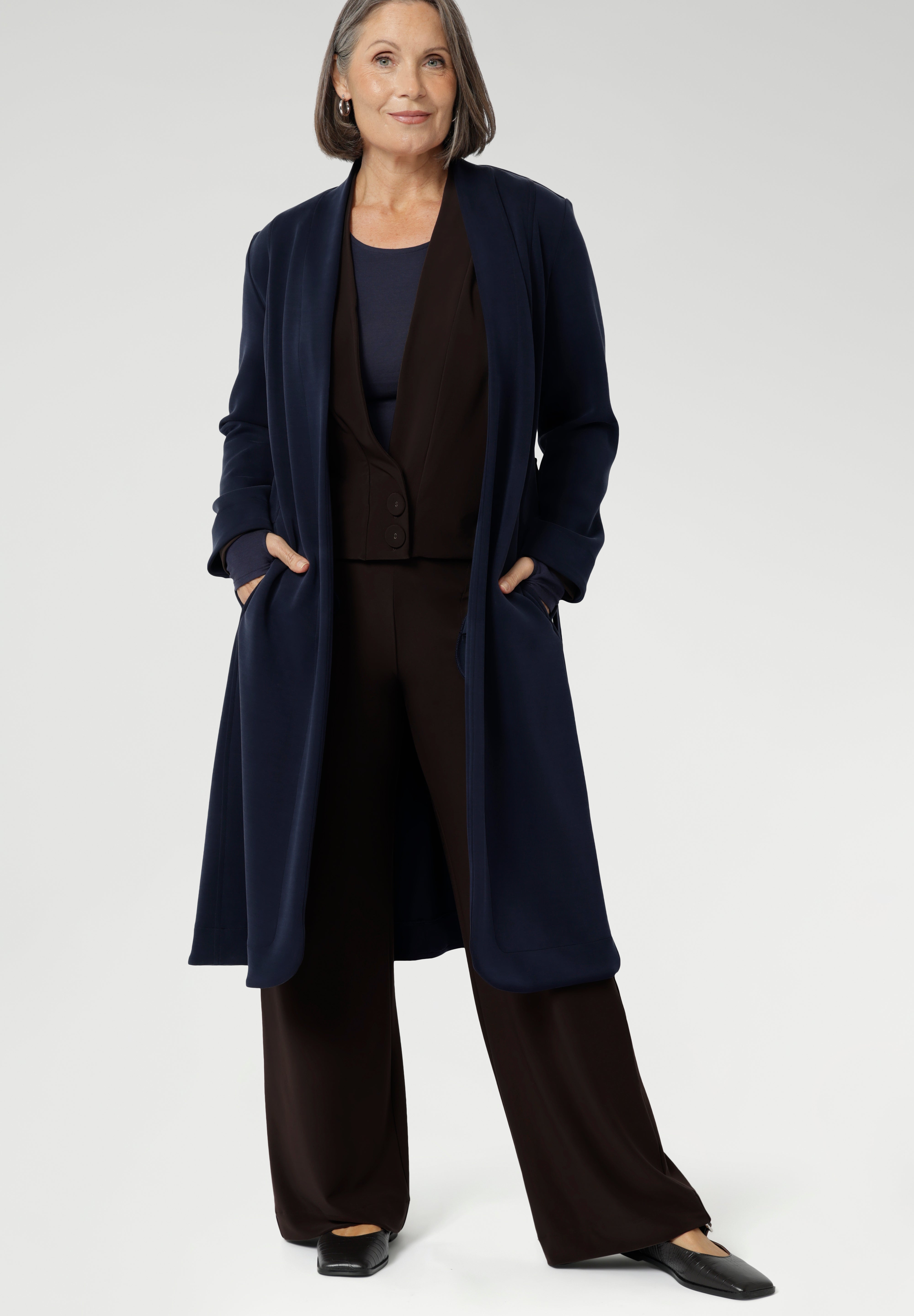 The Sorel Trench Coat is expertly tailored with a modern, sophisticated silhouette that elevates any wardrobe. Mature aged model wears Sorel Trenchcoat in Midnight over fluid suiting for a comfortable and warm travel outfit.