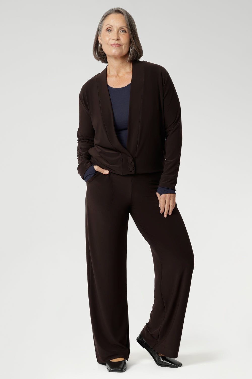 Mature aged woman wears the Sandro Jacardi in Cocoa which is a jacket-like cardigan that effortlessly adds layered dresses, making it an essential piece in our Fluid Suiting collection. Crafted from a heavyweight dry-touch jersey fabric with a soft stretch, this cardigan offers both comfort and structure.