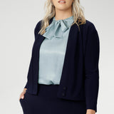 Plus size woman wears navy cardigan paired with woman's navy work pants and blue blouse with neck ties. The Jacardi features long sleeves, this jacket-cardigan hybrid is the perfect trans-seasonal cover up for women. Move into the cooler months in style, with this comfortable jacket for workwear and casual layering. Available in sizes 8-24.