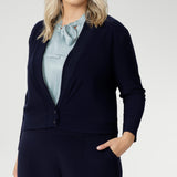 Plus size woman wears navy cardigan paired with woman's navy work pants and blue blouse with neck ties. The Jacardi features long sleeves, this jacket-cardigan hybrid is the perfect trans-seasonal cover up for women. Move into the cooler months in style, with this comfortable jacket for workwear and casual layering. Available in sizes 8-24.