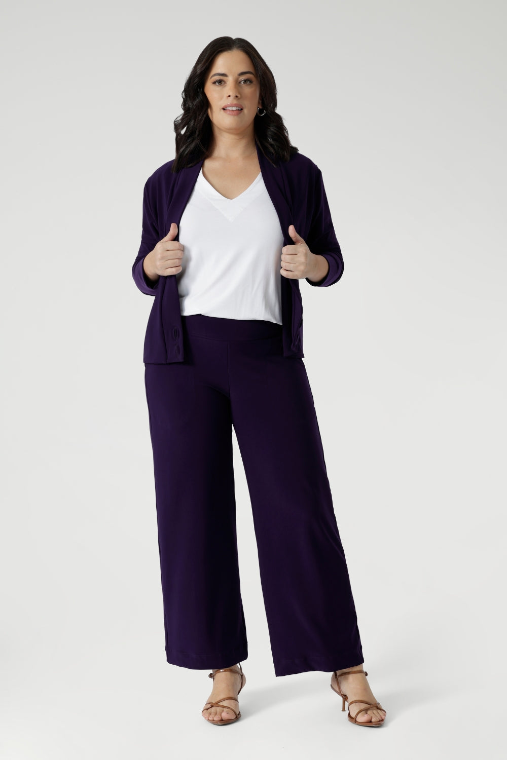 The Sandro Jacardi is a versatile jacket-like cardigan that effortlessly layers over dresses, making it an essential piece for any woman's workwear wardrobe. Petite height model wears purple jacket with matching purple wide leg pants and white top.