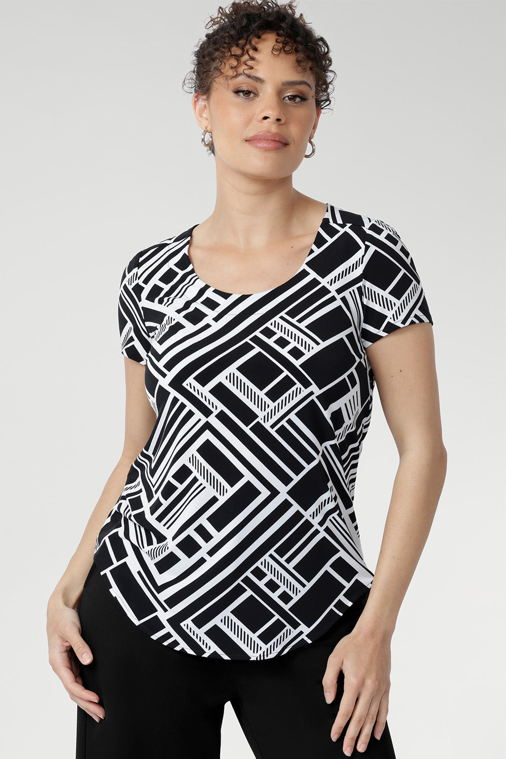 Designed with a flattering fitted silhouette, this versatile top features a classic round neckline, short sleeves, and a curved shirttail hemline that adds a modern touch to any outfit. Available in sizes 8-24