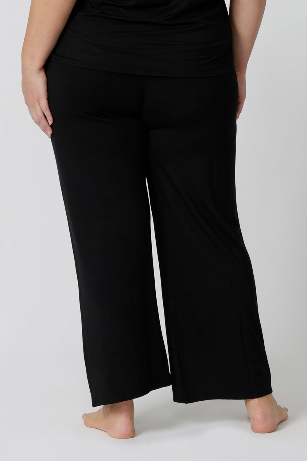 Back view of comfortable loungewear pants in black bamboo jersey. A size 18 woman wears straight wide leg black bamboo lounge pants with a black bamboo slouchy tee top. Thermo-regulating and breathable this is a great pyjama set for night sweats and hot flushes. Shop plus size lounge and sleepwear online at L&F Australia.