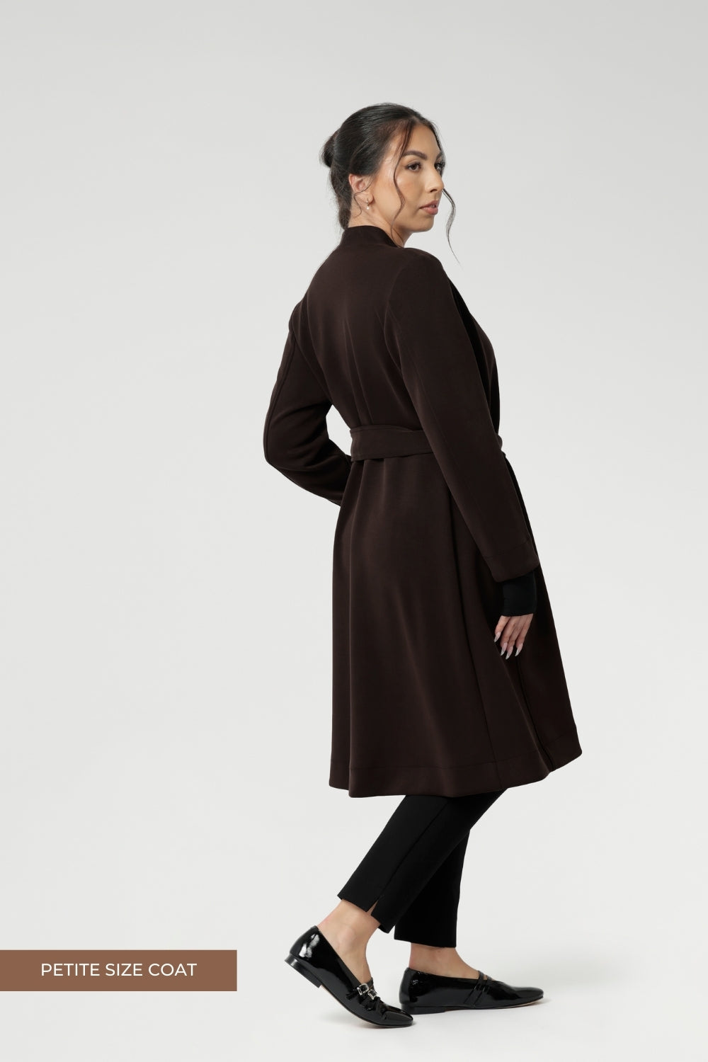 Petite height model wears the Sorel Trench Coat over Paxton Pants & Bryn Top in black for a warmer layer over work wear outfit. The buggy lining at the back ensures added comfort, while the waist seam at the back provides a flattering shape. With belt loops and a fabric waist tie, this versatile trench coat is available in sizes 8-24 and is proudly made in Australia.