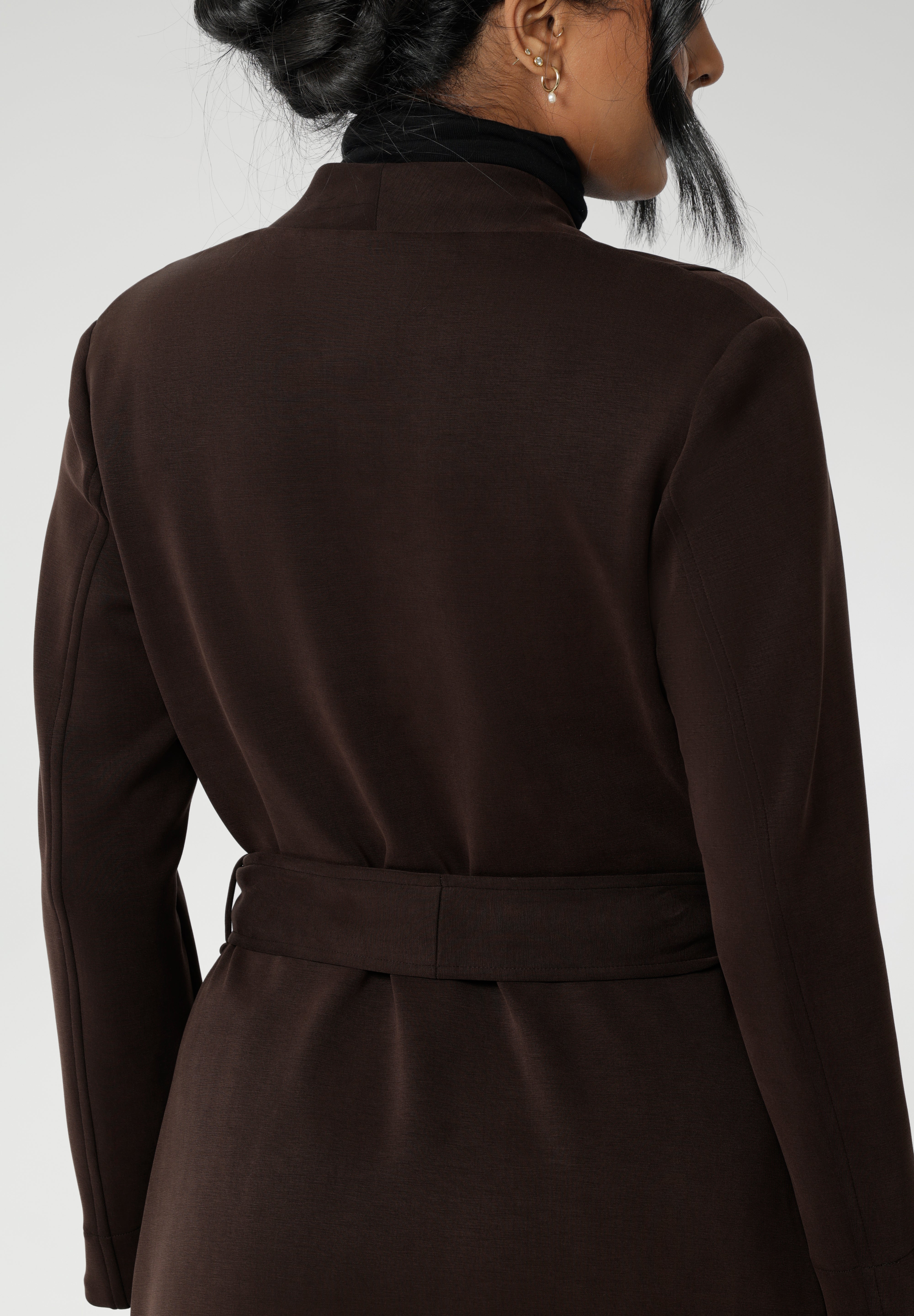 The Sorel Trench Coat is expertly tailored with a modern, sophisticated silhouette that elevates any wardrobe. Size 10 woman wears winter coat crafted from a luxurious winter-weight Modal fabric over long length black pants, black turtle neck, and high heel boots for an elevated workwear look.