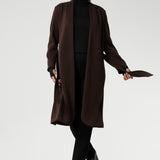 The Sorel Trench Coat is expertly tailored with a modern, sophisticated silhouette that elevates any wardrobe. Size 10 woman wears winter coat crafted from a luxurious winter-weight Modal fabric over long length black pants, black turtle neck, and high heel boots for an elevated workwear look.