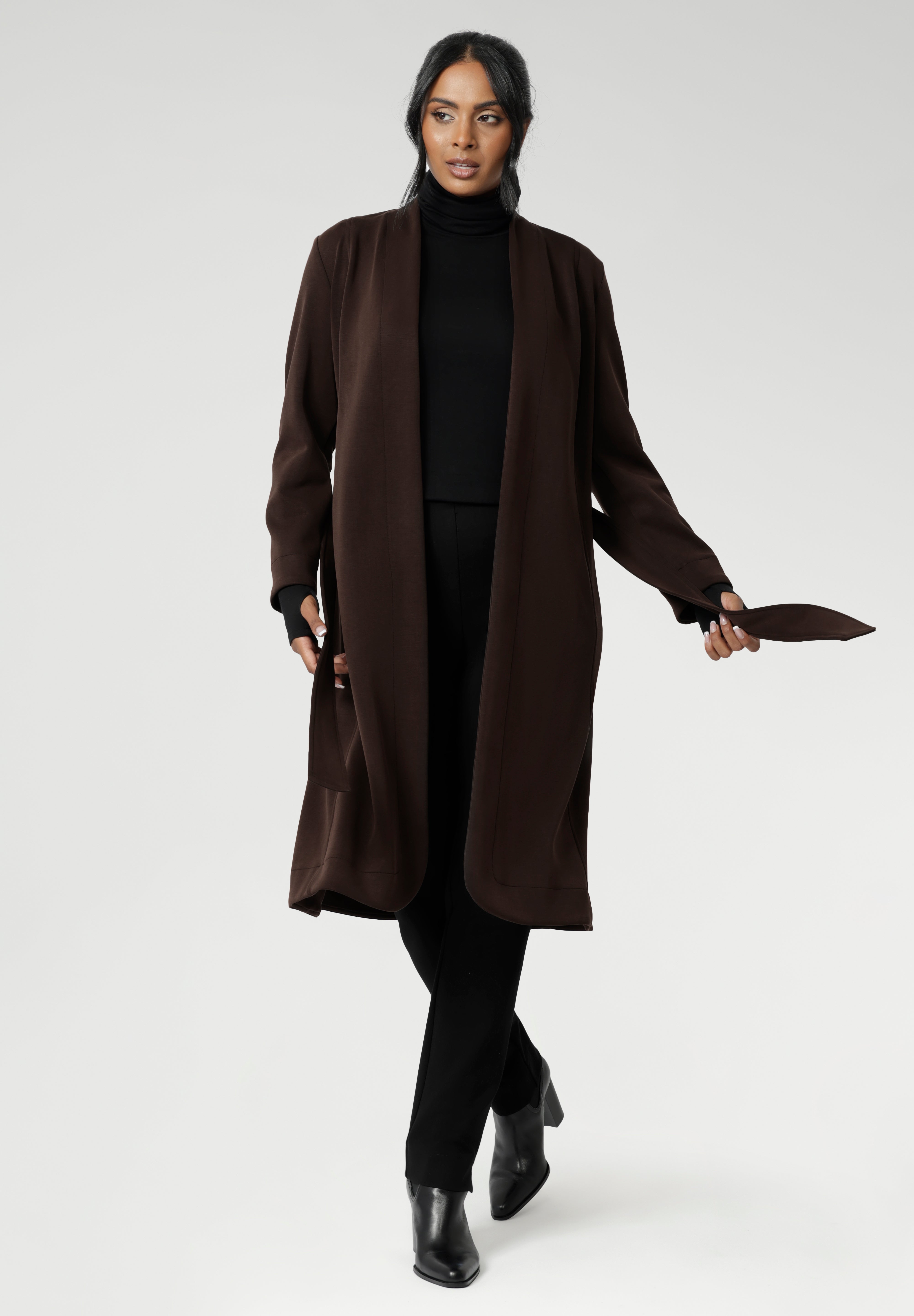 The Sorel Trench Coat is expertly tailored with a modern, sophisticated silhouette that elevates any wardrobe. Size 10 woman wears winter coat crafted from a luxurious winter-weight Modal fabric over long length black pants, black turtle neck, and high heel boots for an elevated workwear look.