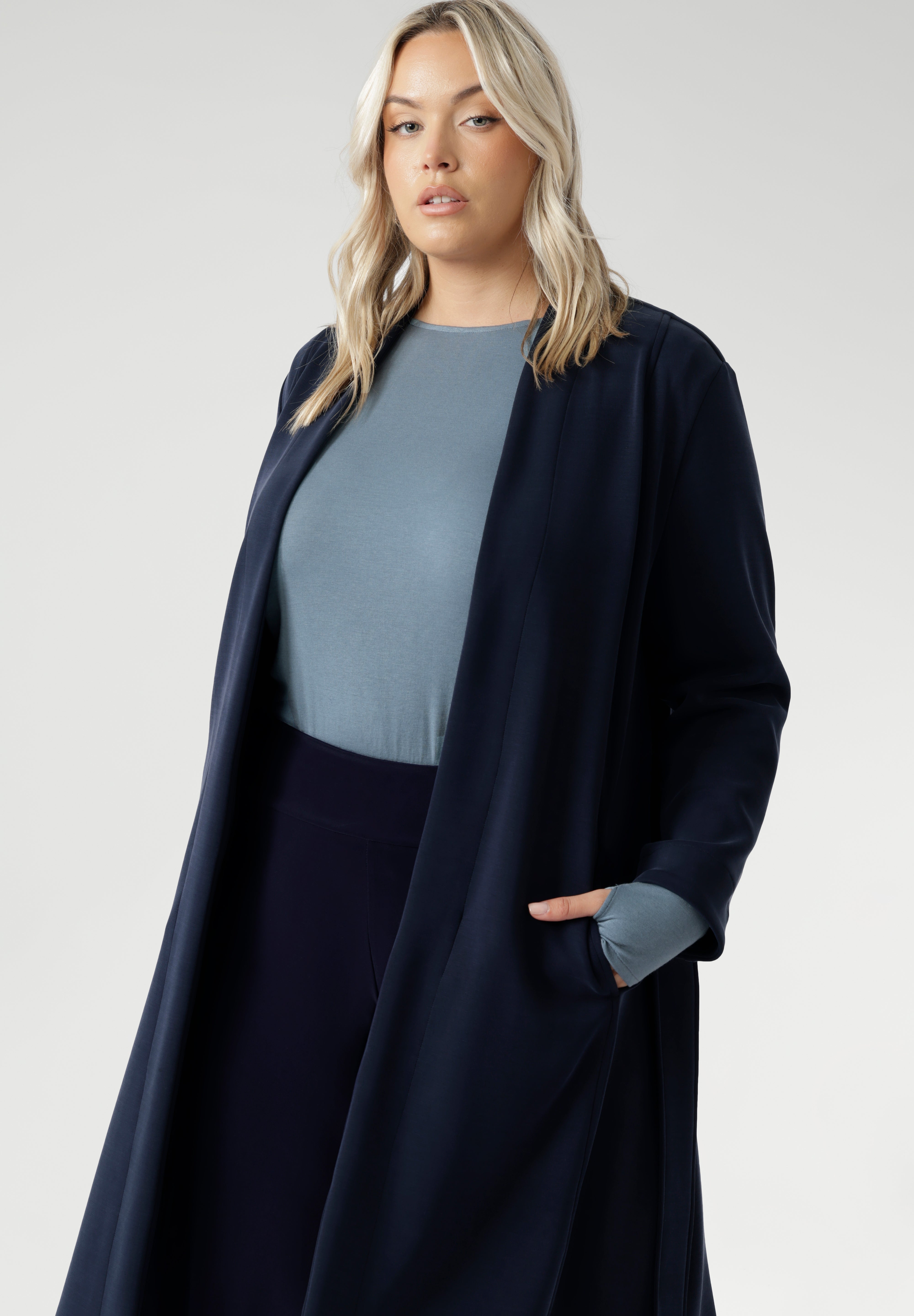 Its grown-on neckline eliminates the need for a collar, offering a sleek, contemporary look. The buggy lining at the back ensures added comfort, while the waist seam at the back provides a flattering shape. With belt loops and a fabric waist tie, this versatile trench coat is available in sizes 8-24 and is proudly made in Australia.