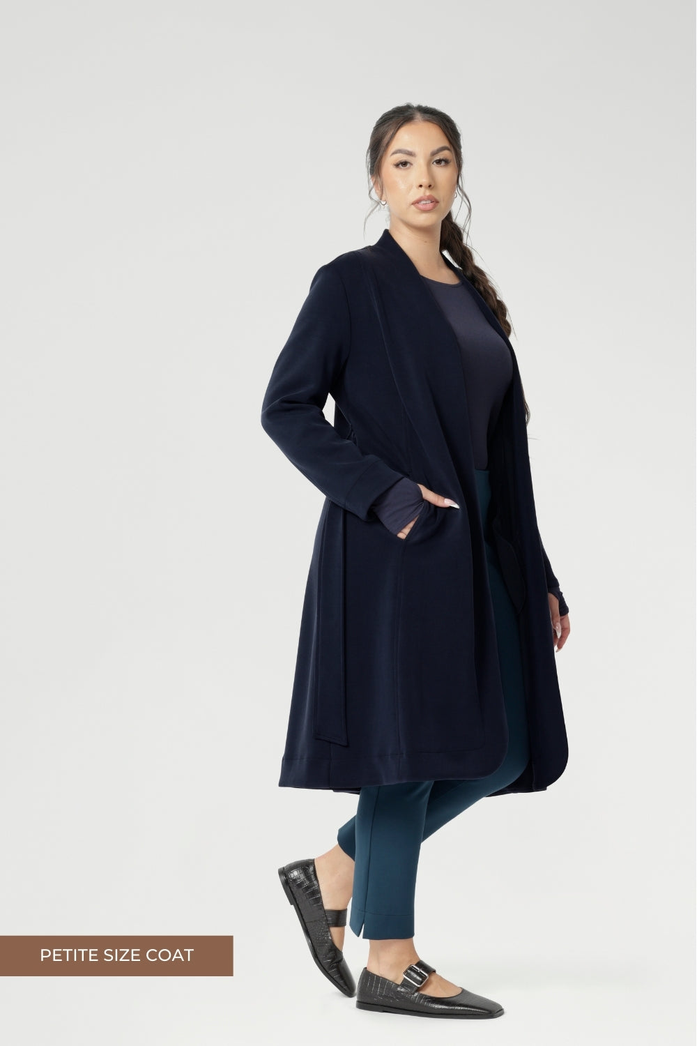 Petite height model wears the Sorel Trench Coat over Paxton Pants & Bryn Top in Navy for a warmer layer over casual workwear look. The buggy lining at the back ensures added comfort, while the waist seam at the back provides a flattering shape. With belt loops and a fabric waist tie, this versatile trench coat is available in sizes 8-24 and is proudly made in Australia.