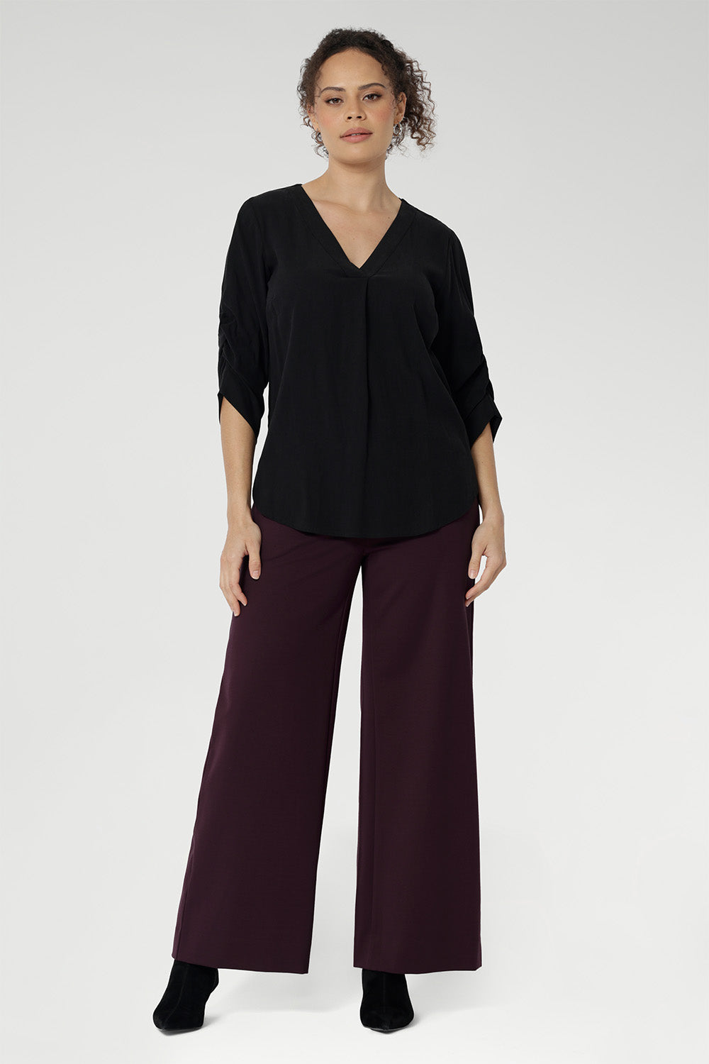 This shirt features a V-neckline with a tailored tuck at the front for a polished look. The back neckline is finished with a facing and a soft pleat that adds subtle detail. The 3/4 length sleeves include elegant ruching that falls toward the centre front of the arm for a refined finish.