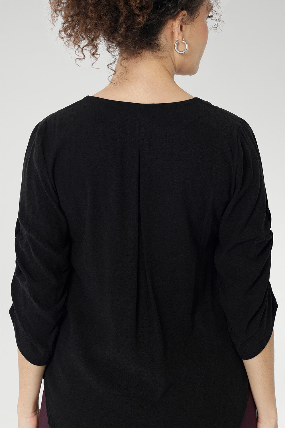 The back neckline is finished with a facing and a soft pleat that adds subtle detail. The 3/4 length sleeves include elegant ruching that falls toward the centre front of the arm for a refined finish.