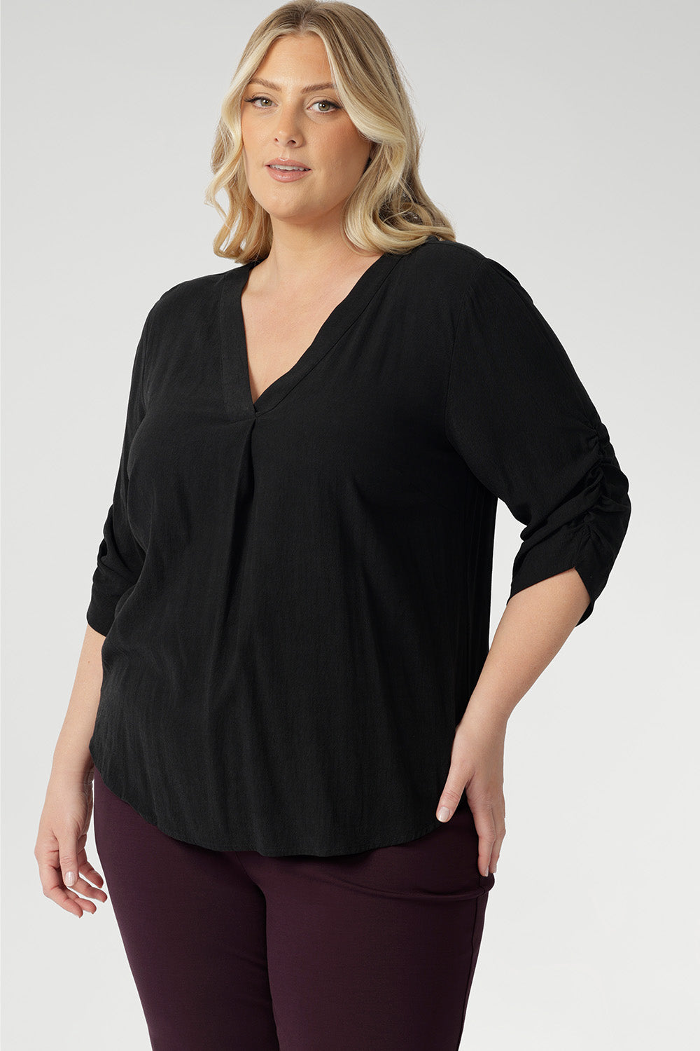 Plus size woman wears 3/4 length sleeve top with elegant ruching details that falls toward the centre front of the arm for a refined finish. She's styled her Terry Shirt in Graphite with wine coloured pants.