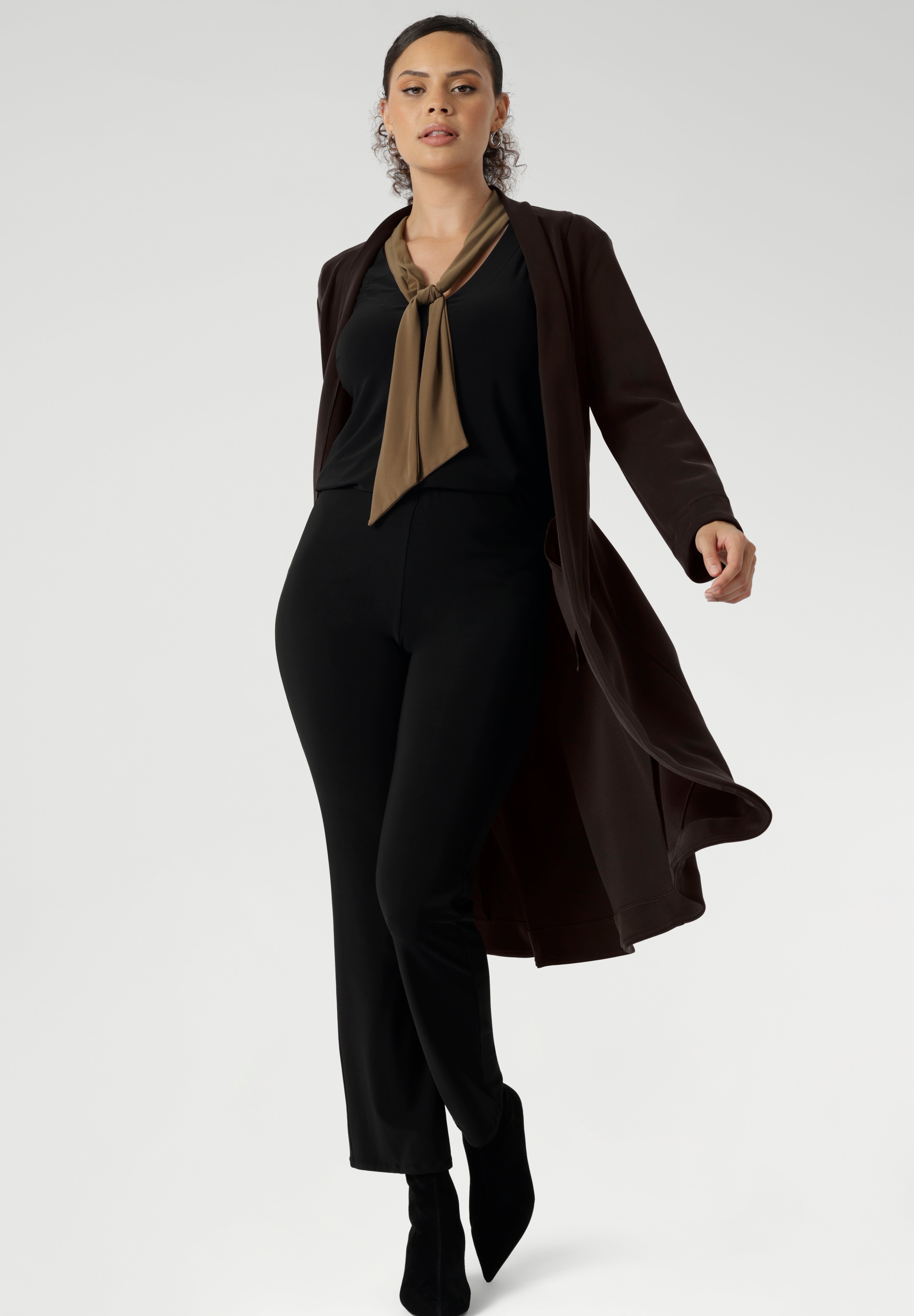 Proudly Australian made, the Thom Top is available in an inclusive size range from 8 to 24, delivering effortless sophistication and comfort for both workwear and special occasions. Over 30's woman wears her Thom Top with black work pants and brown coat.