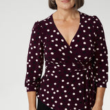Mature aged model wears women's workwear top with flattering peplum silhouette. Its hemline dips gracefully at the back, offering extra coverage and a feminine touch. Available in sizes 8-24. Australian made from dry touch jersey fabric.