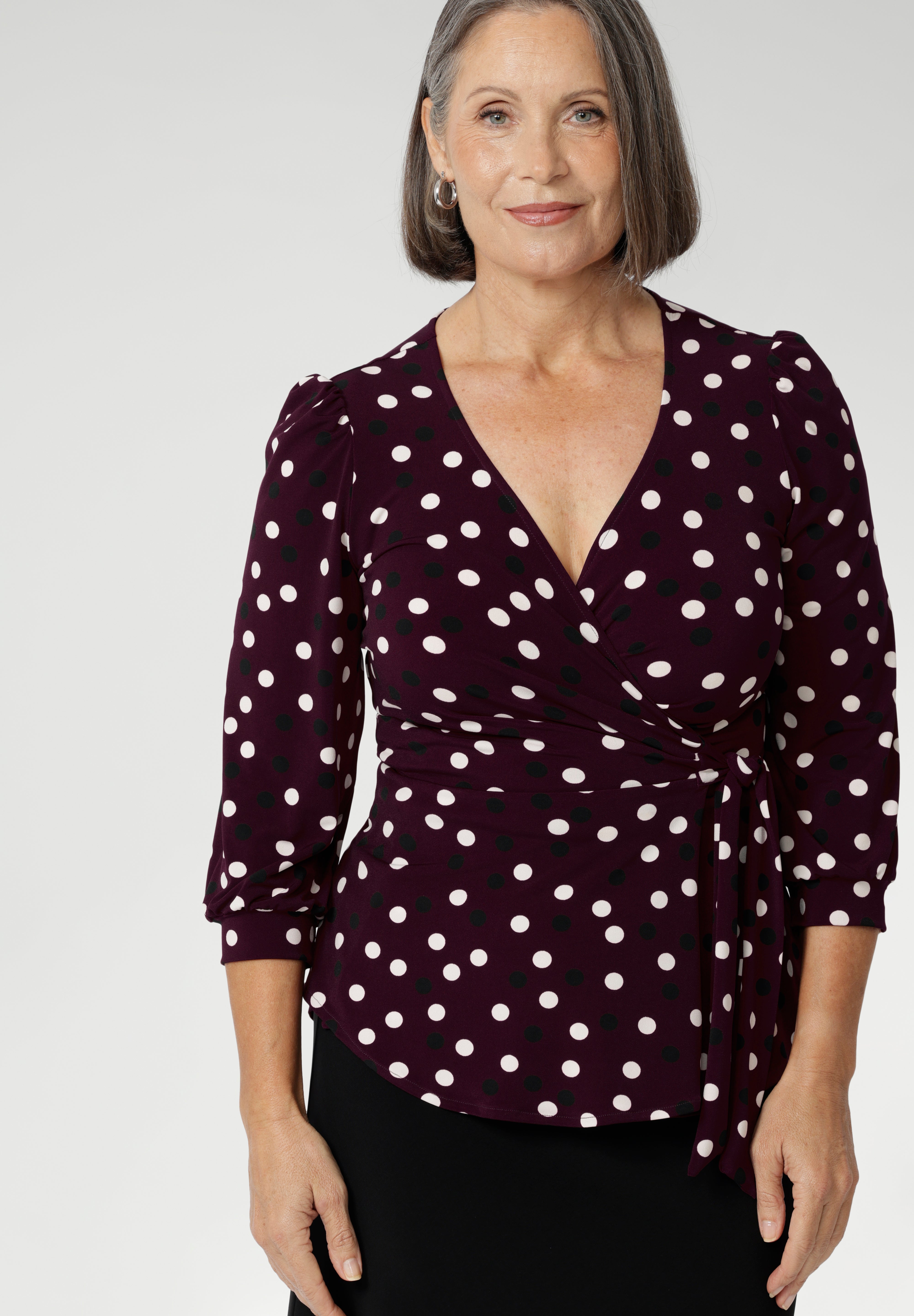 Mature aged model wears women's workwear top with flattering peplum silhouette. Its hemline dips gracefully at the back, offering extra coverage and a feminine touch. Available in sizes 8-24. Australian made from dry touch jersey fabric.
