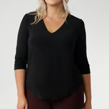 Plus size woman wears the Vida top in black that has a V-neckline and 3/4 sleeve with burgundy suiting set, with matching pants and jacket.