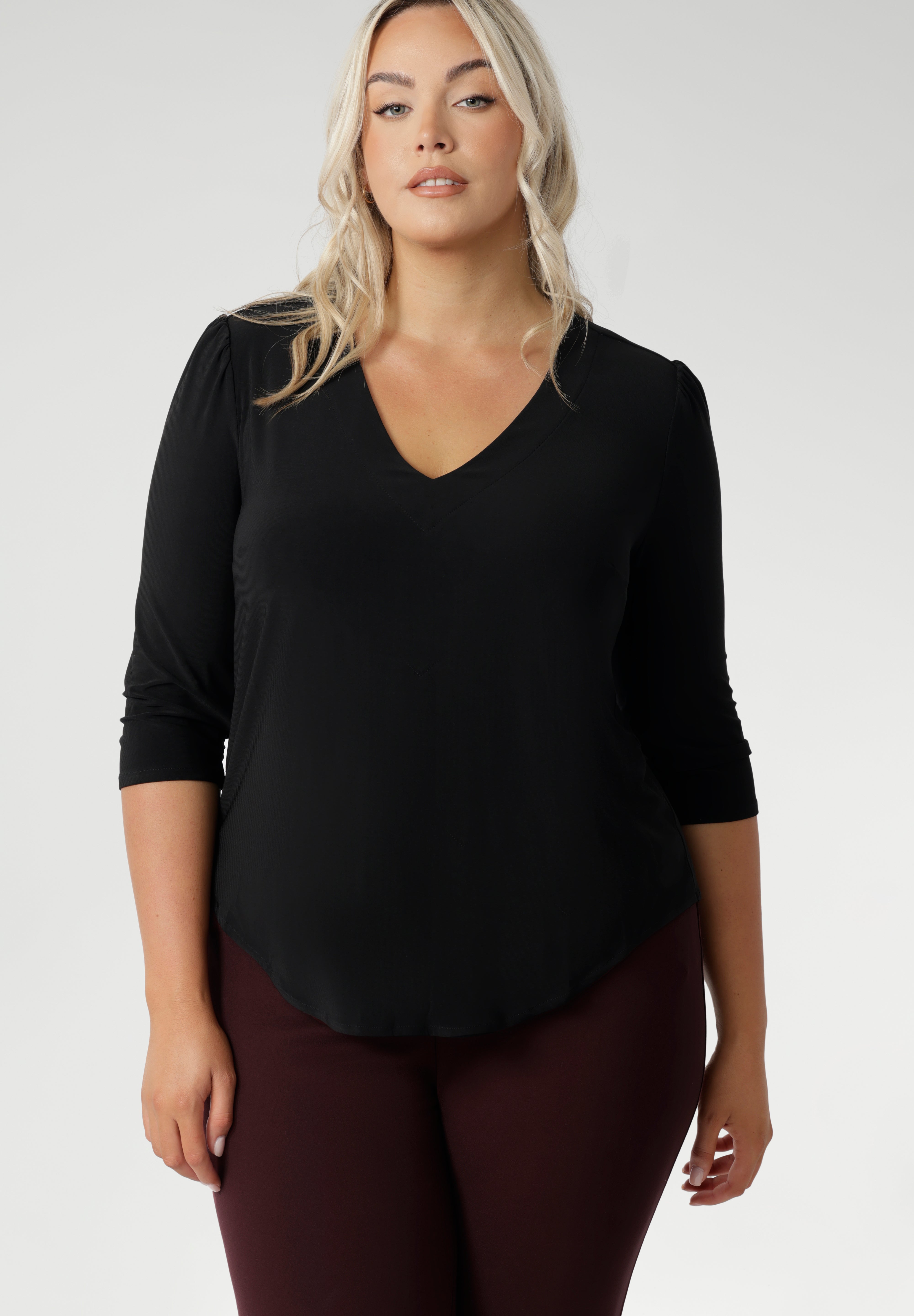 Plus size woman wears the Vida top in black that has a V-neckline and 3/4 sleeve with burgundy suiting set, with matching pants and jacket.
