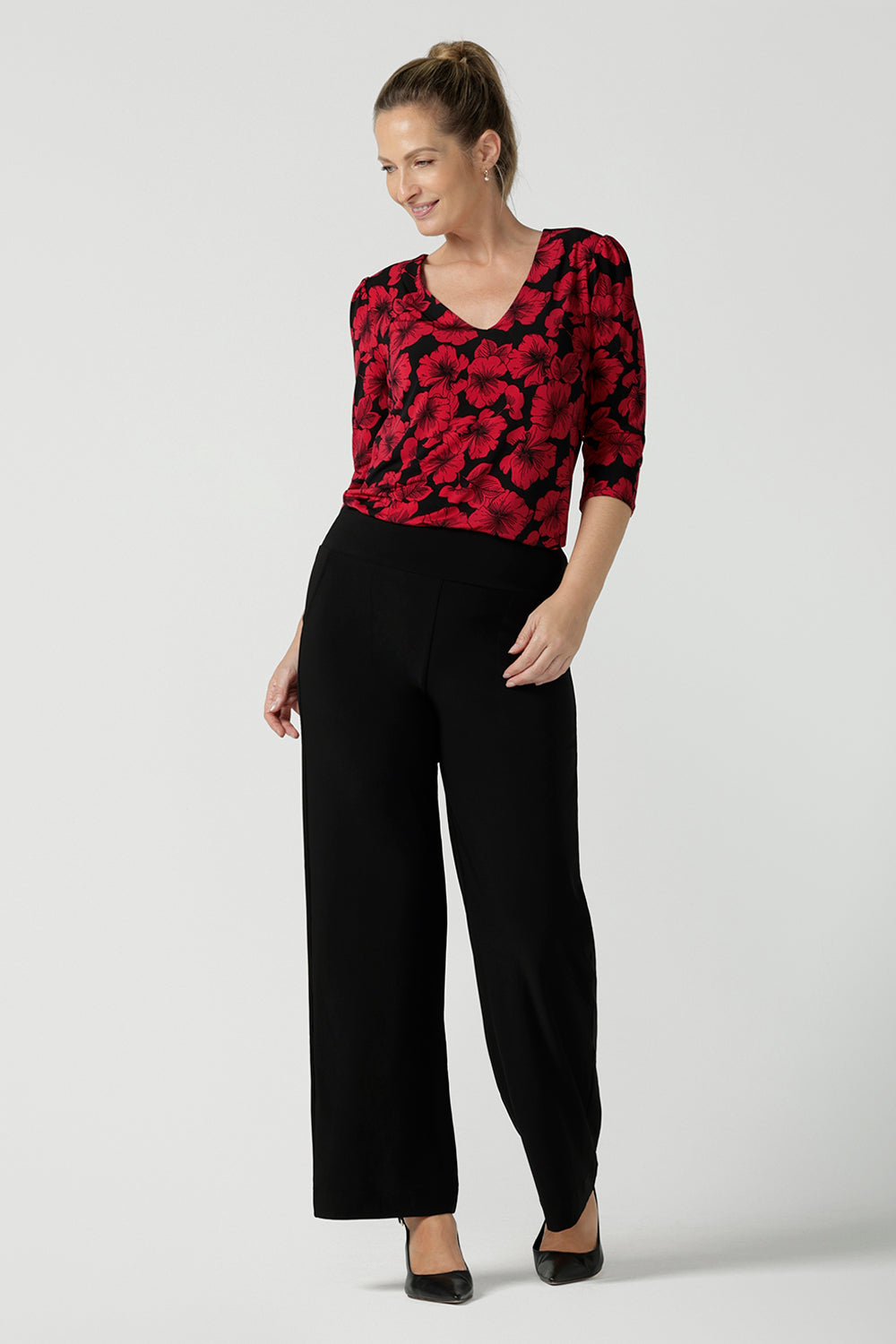 Size 10 woman wears the Vida Top with a v-neck and bold poppy floral. Comfortable workwear top for women size 8 - 24. Black base with a red flower. Versatile and comfortable workwear. Styled back with a black Monroe pants. Made in Australia for women.