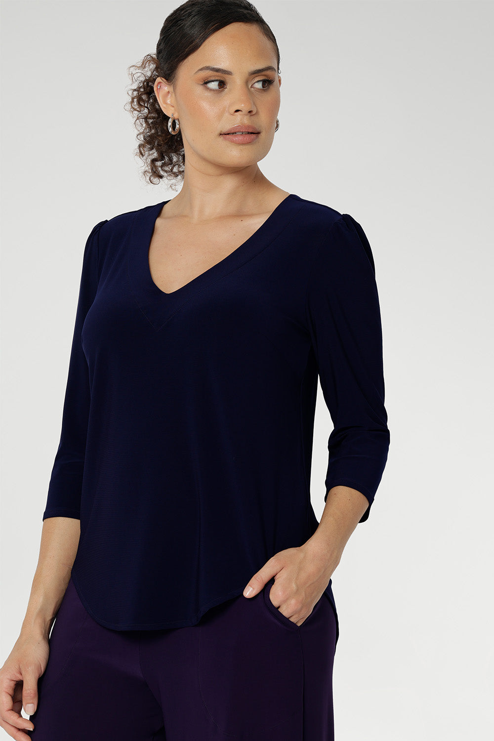 Size 10 woman wears the Vida Top in classic Navy, showcasing its flattering V-neckline and elegant 3/4 sleeves. Crafted from our signature dry-touch stretch jersey, this top offers all-day comfort and effortless style, making it the perfect choice for everything from corporate workwear to relaxed weekend dressing.