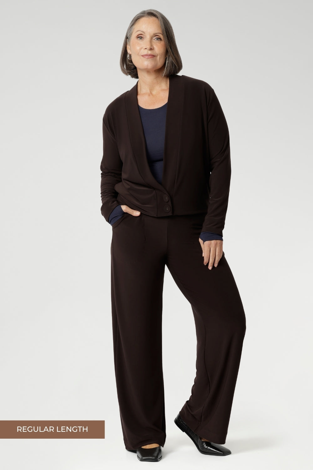 Mature aged model wears Monroe Pants in Cocoa. Crafted from a luxe jersey fabric that drapes beautifully and offers all-day comfort. It pairs perfectly with other pieces from our fluid suiting collection.