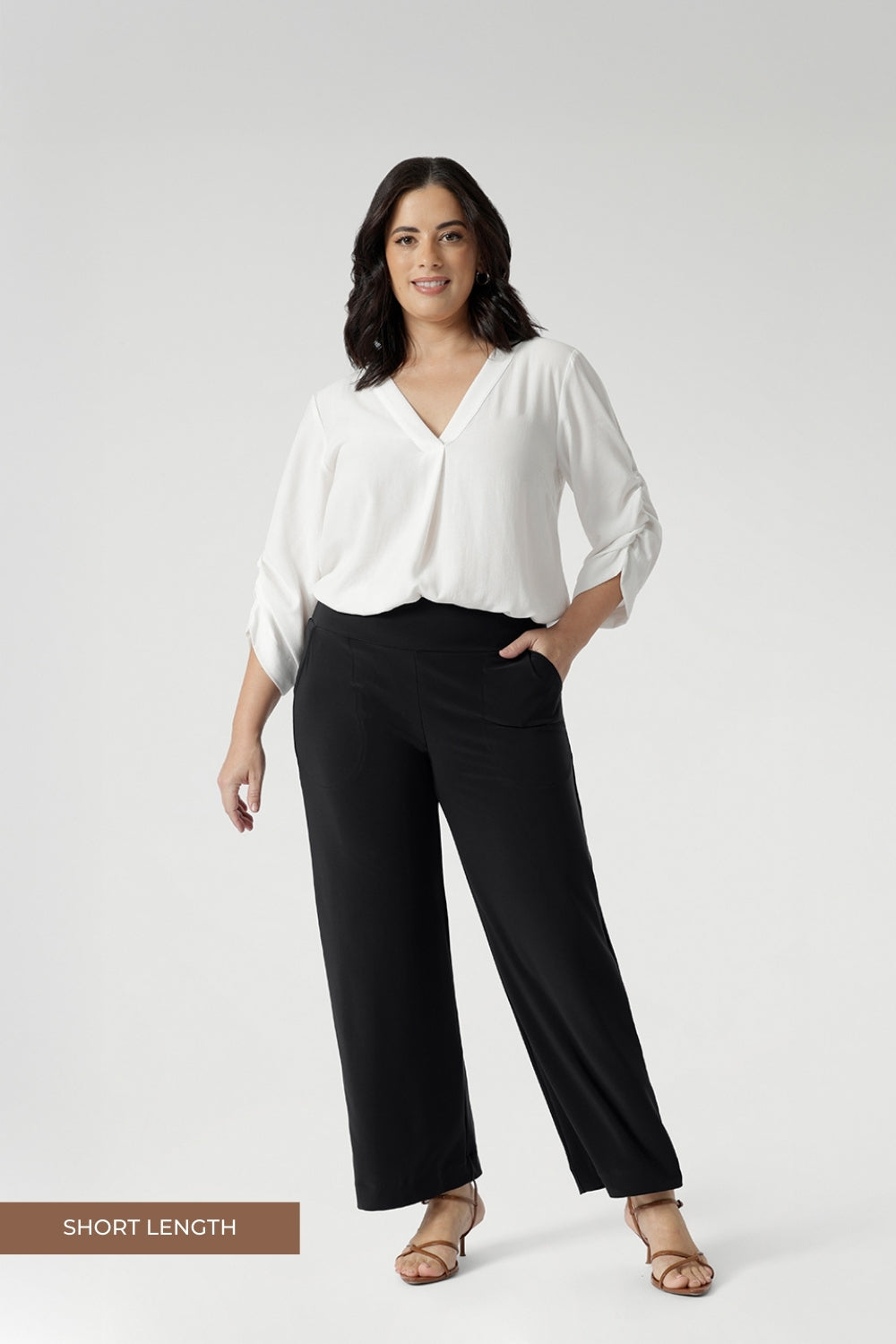 Petite height woman wears pull on workwear pants with vanilla blouse and brown kitten heels. Elevate your workwear with these Australian-made, versatile pants that offer both style and comfort. Charcoal coloured Monroe Pant are available in sizes 8-24 and in 3 leg lengths.