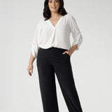 Petite height woman wears pull on workwear pants with vanilla blouse and brown kitten heels. Elevate your workwear with these Australian-made, versatile pants that offer both style and comfort. Charcoal coloured Monroe Pant are available in sizes 8-24 and in 3 leg lengths.