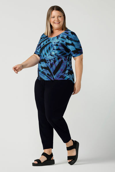 Curvy size 18 woman wears boat neckline Ziggy top in Flutter. A cobalt and purple print on a black base that is digitally printed. Made in Australia in soft Jersey with elbow length sleeves. A great work to weekend top. Size 8 - 24. Styled back with black slim fit Brooklyn pants.