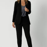 Full body image of 40 year old model wearing black blazer with tuxedo collar. Blazer is made of stretchy scuba crepe fabric. Easy care blazer withstands through daily wear while maintaining a polished look. Black work wear blazer provides the perfect blend of work wear and off-duty style. Australia made clothing. Leina & Fleur stock soft suiting in sizes 8 through to 24. 