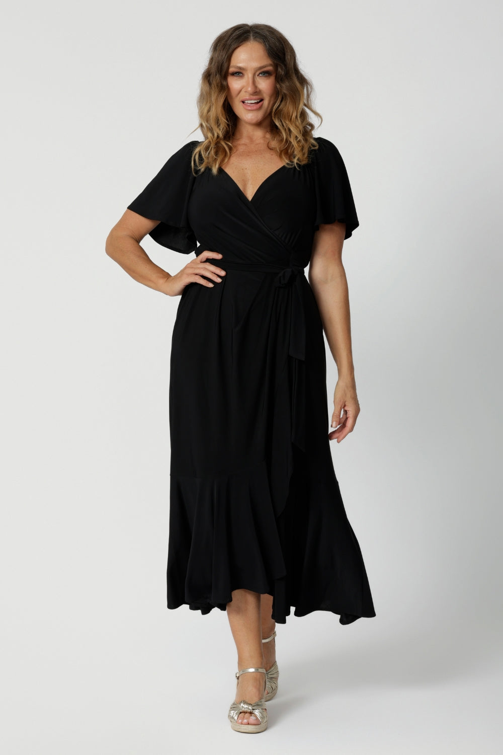 A curvy midsize woman over 40 is wearing a maxi wrap dress in black. Made in Australia by Australian fashion brand Leina & Fleur in sizes 8 to 24.