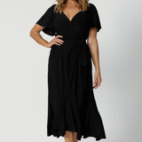 A curvy midsize woman over 40 is wearing a maxi wrap dress in black. Made in Australia by Australian fashion brand Leina & Fleur in sizes 8 to 24.