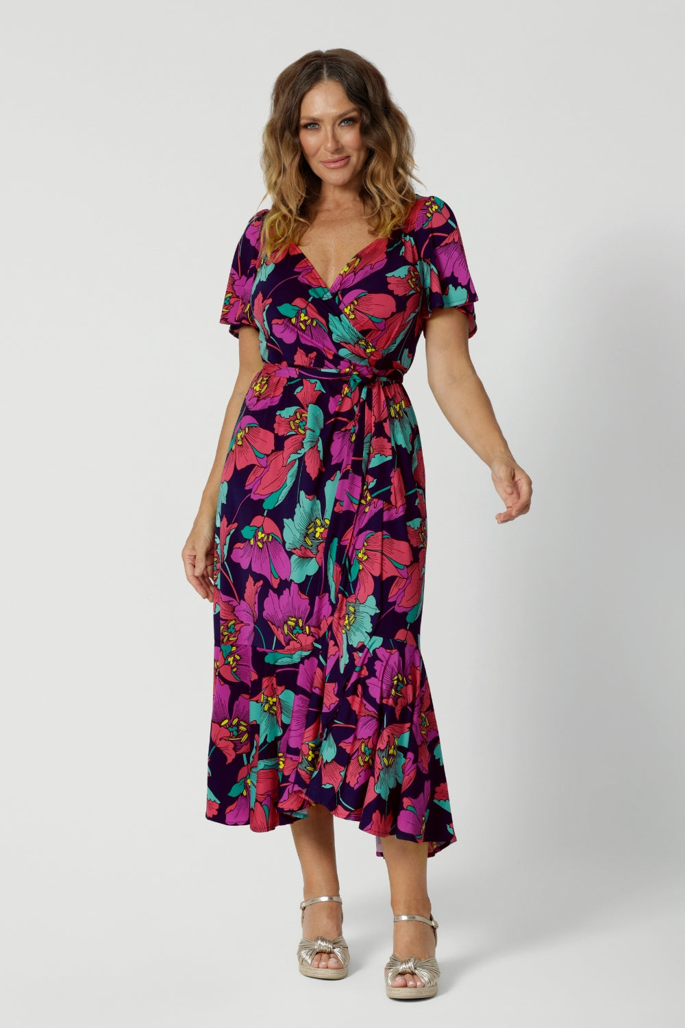 A size 10 woman over 40 wears a maxi wrap dress in a bold print. An elegant wrap dress with a tiered ruffle skirt,  sweetheart neckline and flutter sleeve. Made in Australia for women size 8 - 24 by Leina & Fleur.