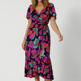 A size 10 woman over 40 wears a maxi wrap dress in a bold print. An elegant wrap dress with a tiered ruffle skirt,  sweetheart neckline and flutter sleeve. Made in Australia for women size 8 - 24 by Leina & Fleur.