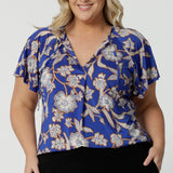 Wearing a summer top for plus size women with flutter sleeves, a curvy size 18 woman shows the relaxed fit of this jersey top. With a holiday print and lightweight, easy care fabric, this is the perfect top for travel and cruisewear. Made in Australia by Australian and New Zealand women's clothes label, Leina & Fleur shop plus size tops online.