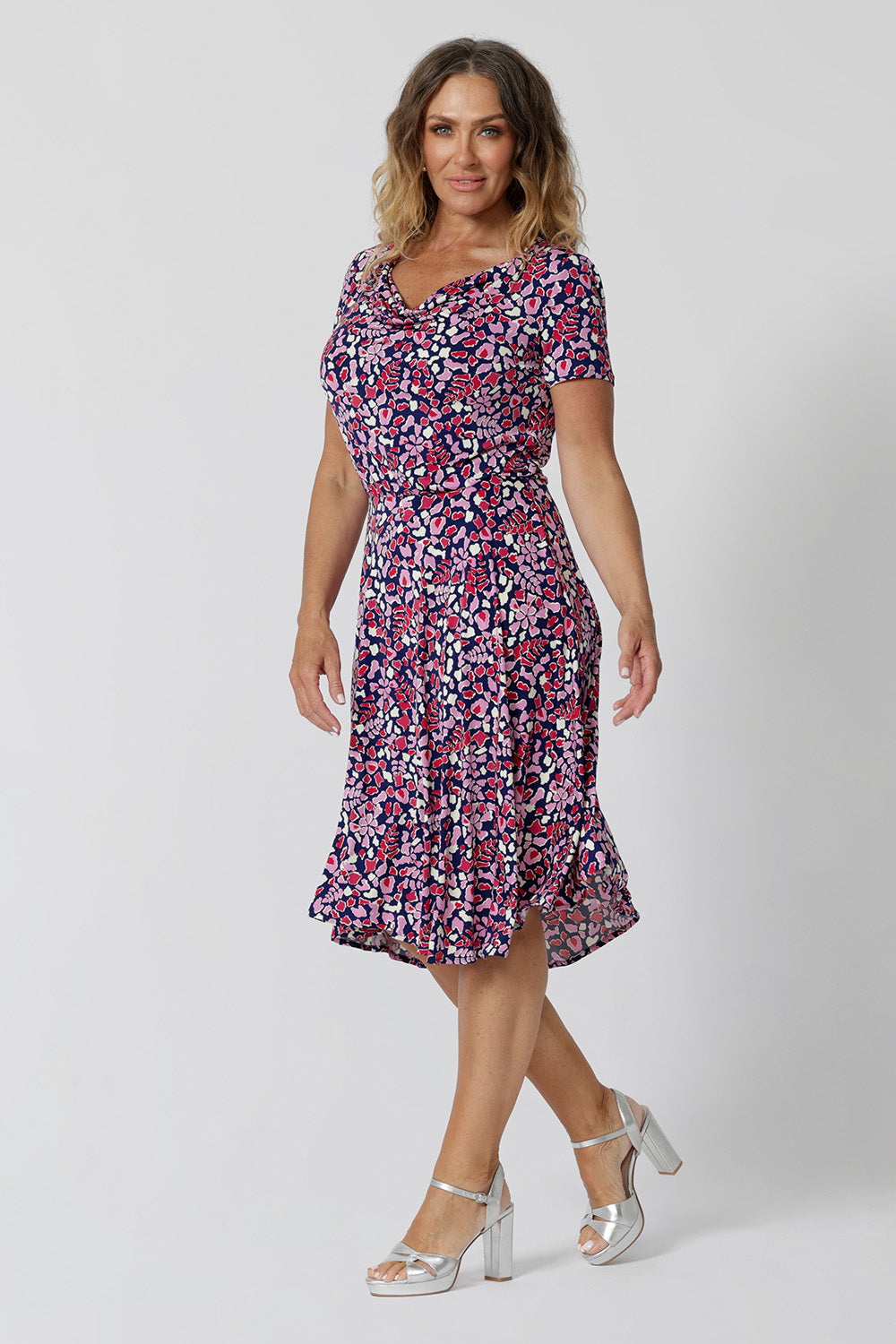 Summer dresses for over 40s women don't get much beter than this! A size 12, over 40 woman wears knee length summer dress with asymmetric hemlineand cowl neck. A short sleeve dress in pretty red, pink, white and navy print this is a good jersey dress for travel and cruise wear.  Shop Australian-made dresses by L&F online as petite to plus size dresses online. 