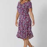 Summer dresses for over 40s women don't get much beter than this! A size 12, over 40 woman wears knee length summer dress with asymmetric hemlineand cowl neck. A short sleeve dress in pretty red, pink, white and navy print this is a good jersey dress for travel and cruise wear.  Shop Australian-made dresses by L&F online as petite to plus size dresses online. 