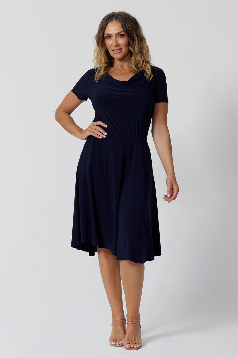 Summer dresses for over 40s women don't get much beter than this! A size 12, over 40 woman wears knee length summer dress with asymmetric hemlineand cowl neck. A short sleeve dress in navy jersey fabric, this is an easy-care dress and makes a good jersey dress for travel and cruise wear.  Made in Australia by Australian and New Zealand women's clothes brand, Leina & Fleur, shop their petite to plus size dresses online. 