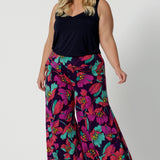 A curvy size 18 woman wears the Caspian Palazzo pant in a bright floral print. In soft and lightweight jersey this pant features side pockets and a flared leg opening. Handmade in Australia in sizes 8-24 by Leina & Fleur.