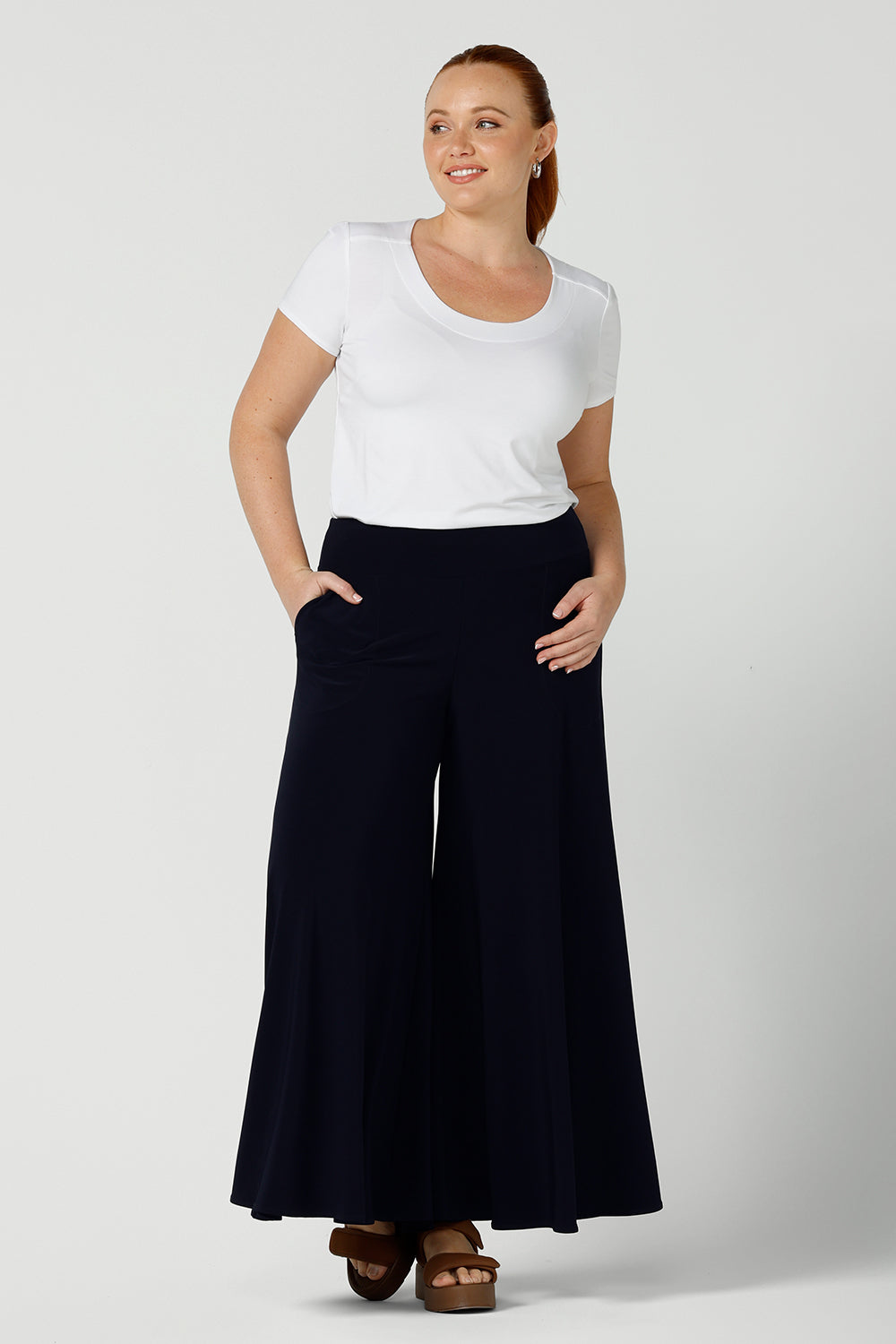 A curvy size, size 12 woman wears wide leg pants with pockets with a white bamboo top. These pull-on, easy care pants are comfortable for your everyday workwear capsule wardrobe. Shop these Australian-made wide leg trousers online in sizes 8 to 24, petite to plus sizes.