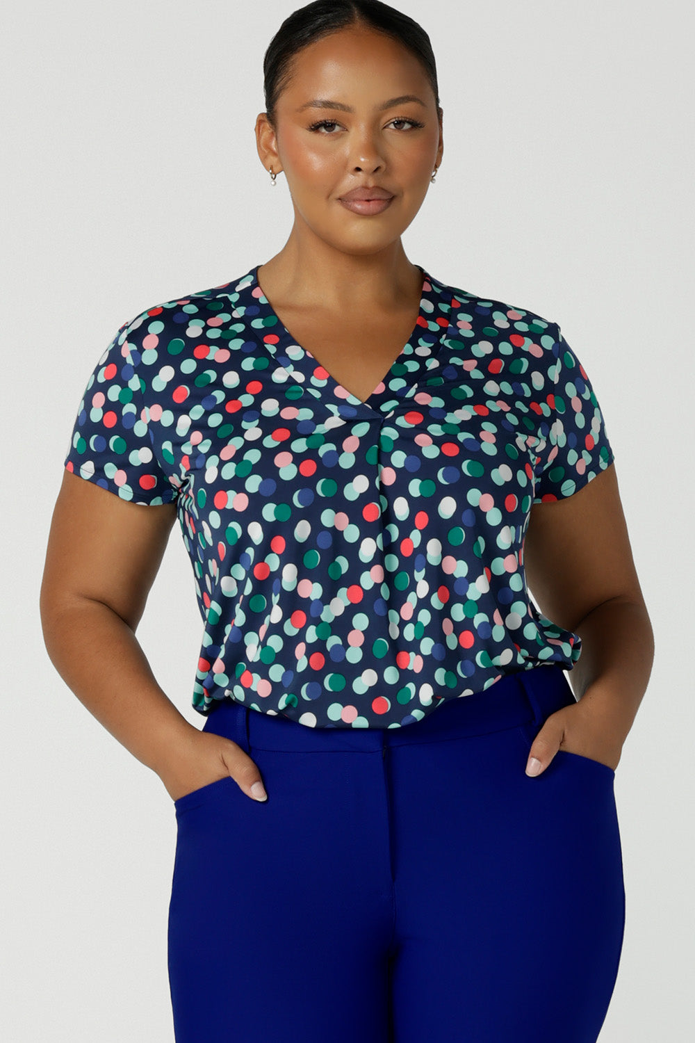 A size 18 woman wears a great top for plus size women's workwear. This V-neck, short sleeve jersey top features a bubble spot print and has a navy base. Made in Australia by Australian and New Zealand women's clothing brand, this workwear top is available to shop online in sizes 8 to 24.