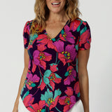 A curvy size 10 woman over 40 wears a top with a v-neckline and short sleeves. It has a bold floral print. The top is handmade in Australia by Australian fashion brand Leina & Fleur in sizes 8 to 24. 