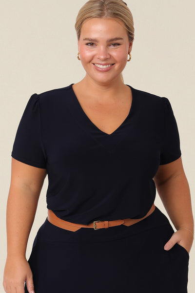 A petite woman with curve wears a navy blue V-neck top with short sleeves. A good work top for plus size women, this tailored top is made in Australia by Australian fashion brand, Leina & Fleur in sizes 8 to 24.