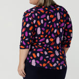 Back view of a size 18 curvy woman wears the Jaime top in Palette. A brush stroke inspired abstract print on a navy base with fuchsia, red, orange and pink spots. A v-neck pleat front top great for work to weekend. Comfortable jersey and easy care. Made in Australia for women size 8 - 24.