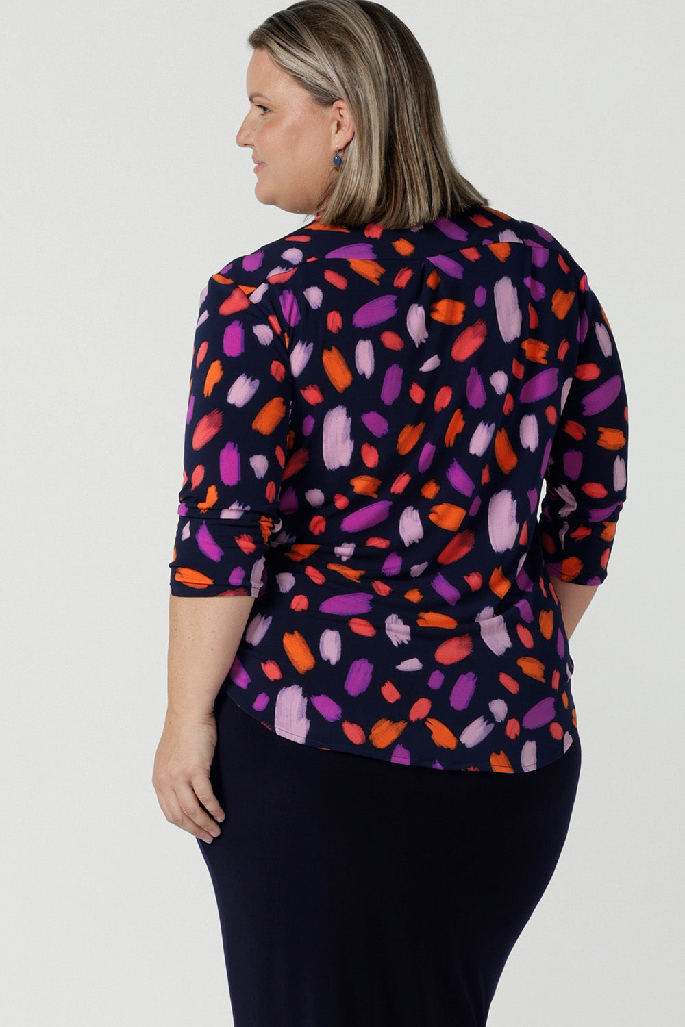 Back view of a size 18 curvy woman wears the Jaime top in Palette. A brush stroke inspired abstract print on a navy base with fuchsia, red, orange and pink spots. A v-neck pleat front top great for work to weekend. Comfortable jersey and easy care. Made in Australia for women size 8 - 24.