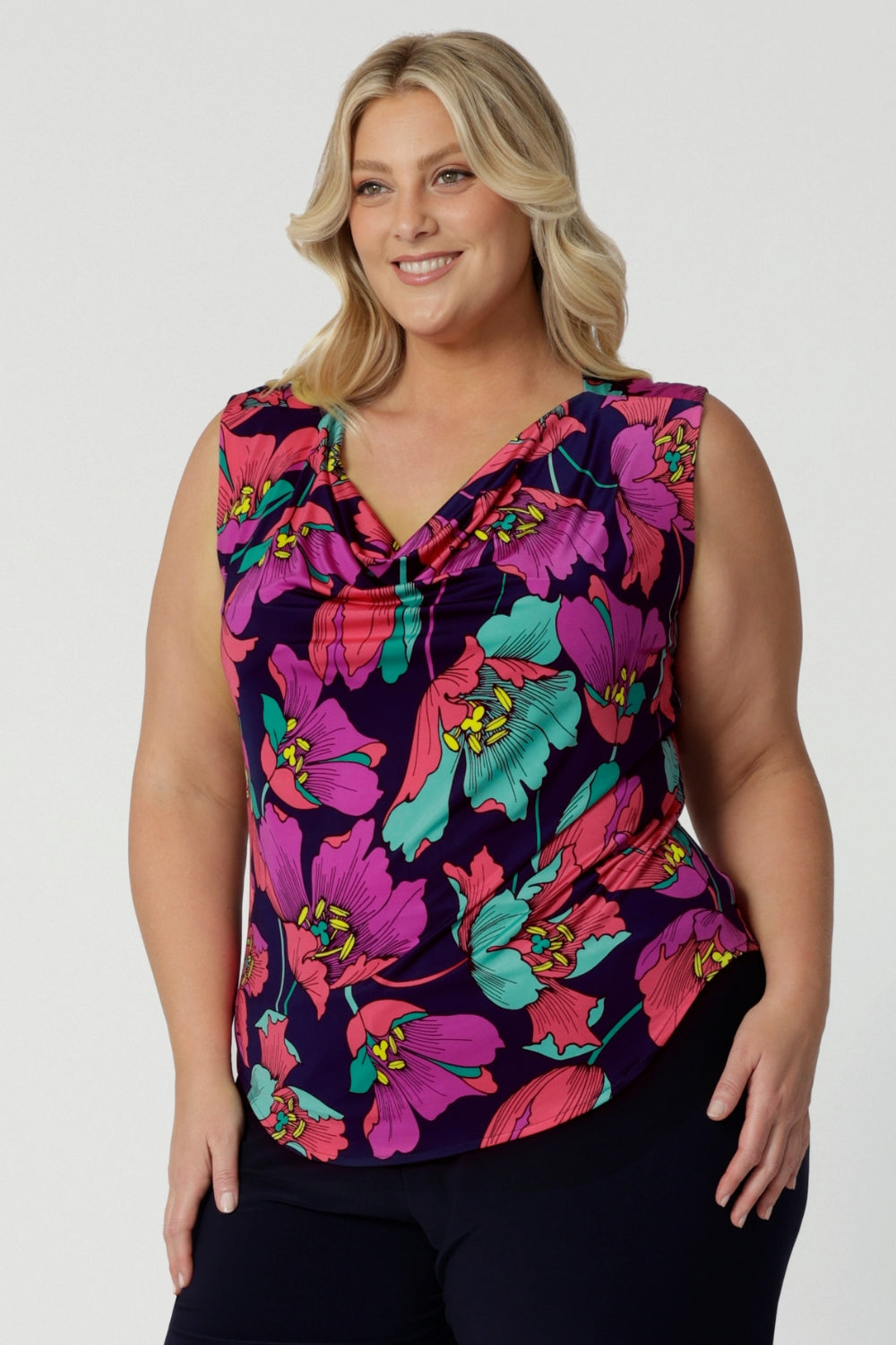 Showing a summer top for curvy women, a size 18, plus size women wears a cowl neck jersey top. This sleeveless top has a bold floral print - great for corporate wear as well as casual wear. Made in Australia by Australian and New Zealand clothing brand, Leina & Fleur, shop this top in petite to plus sizes. 