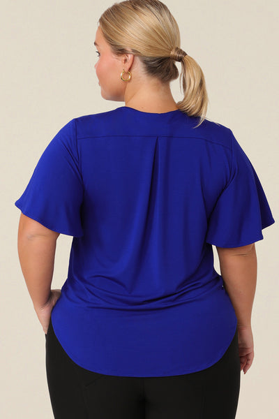 Back view of a A plus size, size 14 woman wearing a V-neck blue top with short flutter sleeves. Made from bamboo jersey, this is a natural fibre top that is lightweight, breathable and sustainable.
