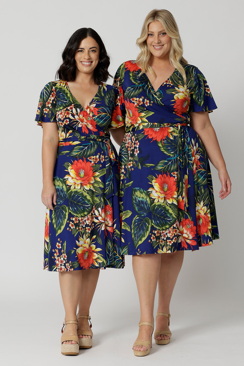 Two women of different heights wearing the Maggie Knee Length Dress in Bahagia. Floral wrap dress is stocked in petite and plus sizes. This resort ready dress is made from blue slinky jersey fabric. This resort style dress is perfect for travel as the fabric is wrinkle resistant and packs well in a suitcase. Leina & Fleur stock many resort style dresses and tops in sizes from 8 to 24.