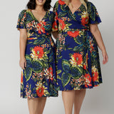 Two women of different heights wearing the Maggie Knee Length Dress in Bahagia. Floral wrap dress is stocked in petite and plus sizes. This resort ready dress is made from blue slinky jersey fabric. This resort style dress is perfect for travel as the fabric is wrinkle resistant and packs well in a suitcase. Leina & Fleur stock many resort style dresses and tops in sizes from 8 to 24.