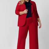 A size 18 woman wears the Merit Blazer in Flame, a textured scuba crepe plus size blazer with button front. This red work blazer is worn with red workwear pants and navy work top. Curved hemline and front pockets. This blazer is Made in Australia for curvy women size 8 - 24.