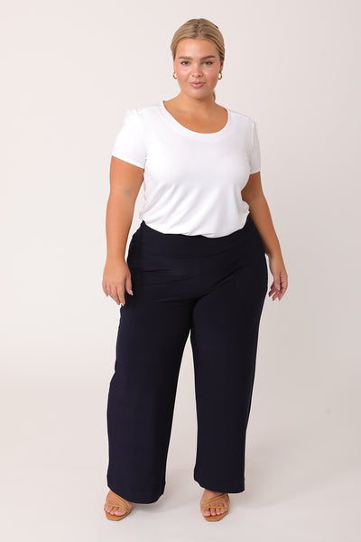 A curvy petite height woman wears navy work pants in petite length with a white bamboo jersey T-shirt top. Great pants for short women, these Australian-made pull-on navy trousers are available in sizes 8 to 24, petite to plus sizes.